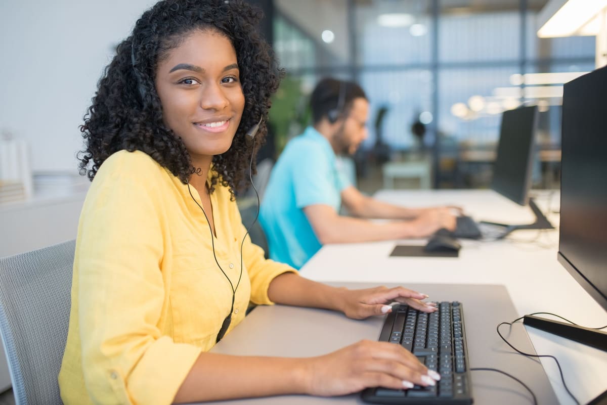 Friendly customer support agent wearing a headset and smiling at her computer
