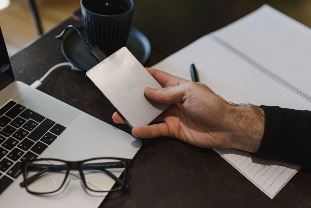 Hand holding an external drive connected to a laptop to back up website files