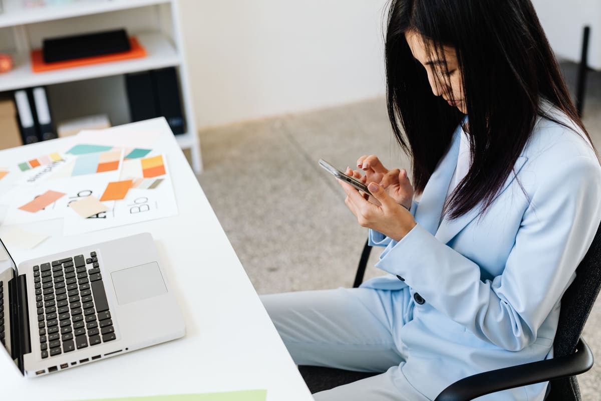 Professional woman checking her business email on a smartphone beside her laptop