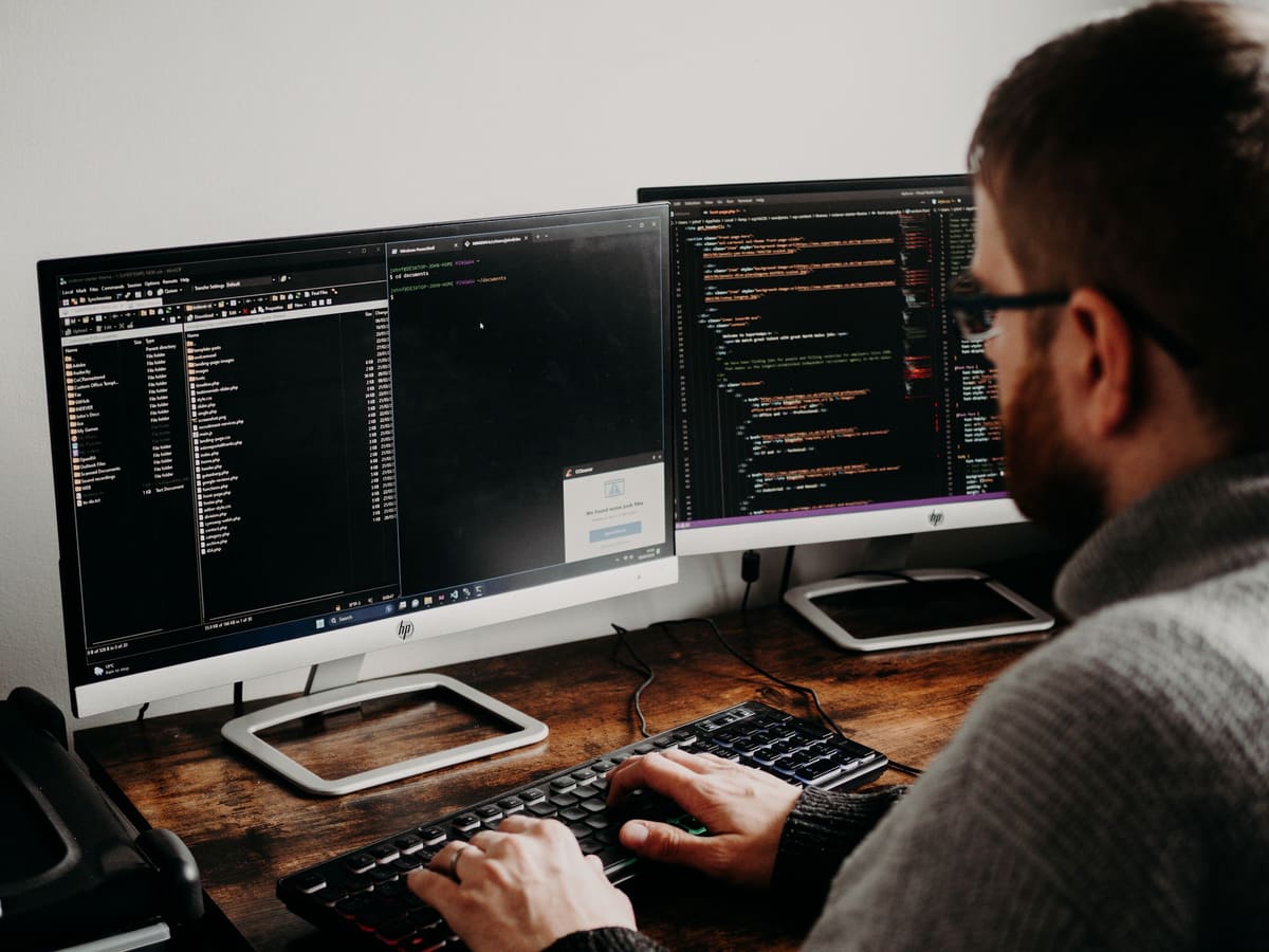 Web developer writing code across two monitors at a wooden desk