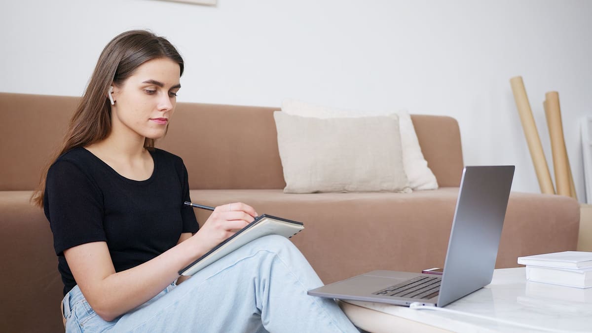 Woman learning at home, taking notes beside her laptop